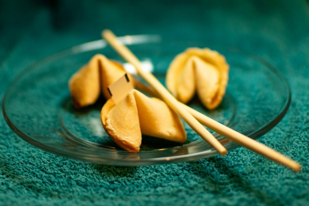Three fortune cookies on a clear glass plate with chopsticks.